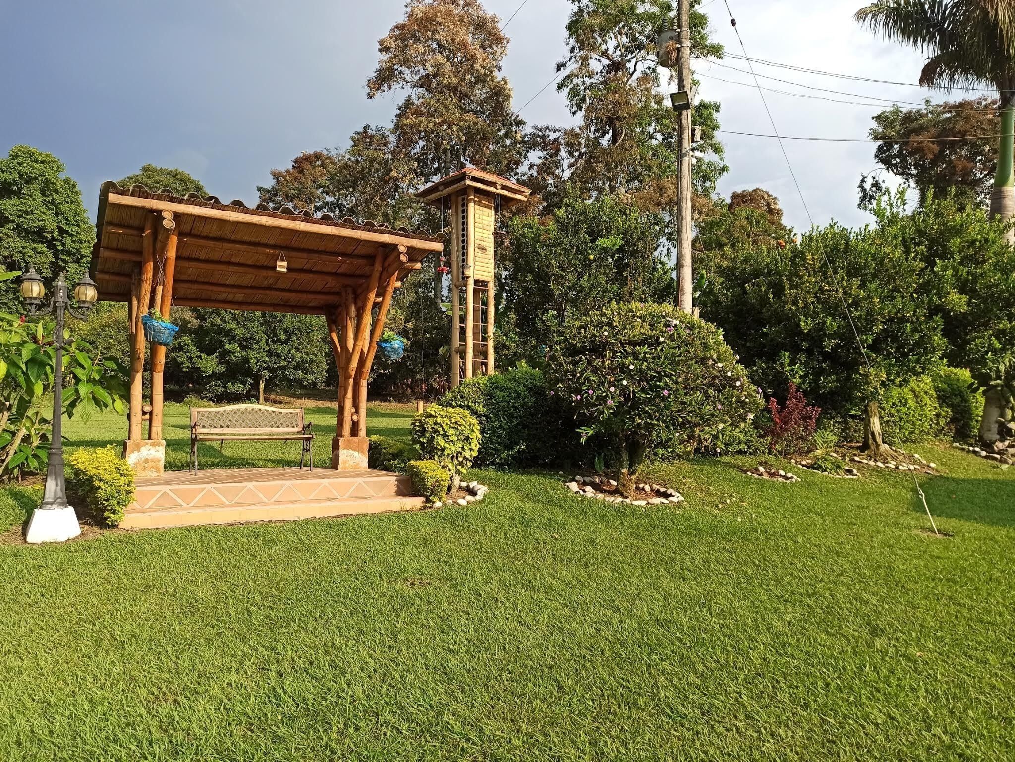 A wooden gazebo with a bench, surrounded by well-maintained grass and various shrubs.