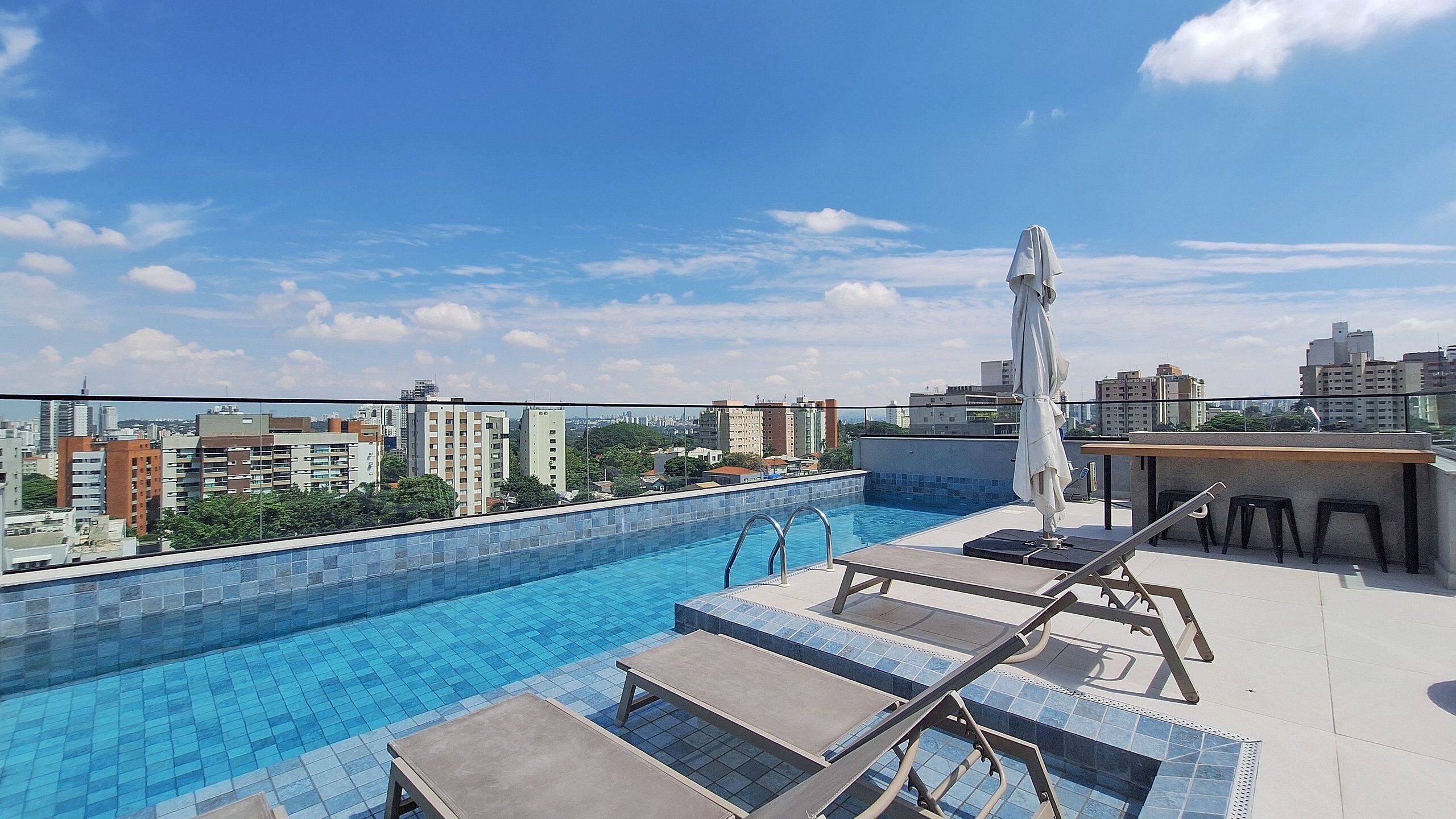 A rooftop pool with lounge chairs and a table, surrounded by a cityscape view.