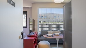 A modern room with a sofa, a dining table set for two, and a balcony with a view of a building. - Vida Madalena (Sao Paulo)