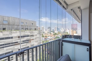 A balcony with a city view, a modern building with a wooden facade, and a glass railing.