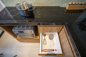 Eine Küche mit schwarzem Arbeitsplatz, einem Topf auf einer Induktionskochplatte, einer Schublade mit Küchenutensilien und einem Gewürzregal.