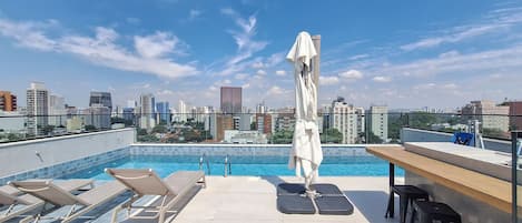 A rooftop pool with lounge chairs and a table, offering a city view.