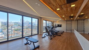 A spacious gym with large windows, exercise equipment, and a city view. - Vida Madalena (Sao Paulo)