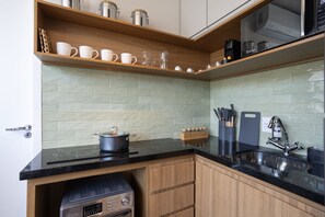 A kitchen with a black countertop, wooden cabinets, a stove, a sink, and a shelf with kitchenware.