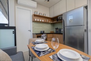 A compact kitchen with a built-in refrigerator, wooden shelves with kitchenware, and a dining area with a table set for two. - Vida Madalena (Sao Paulo)