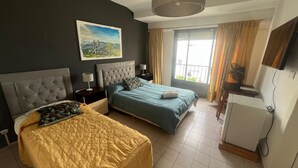 Een hotelkamer met twee bedden, een schilderij aan de muur, een raam met gordijnen en een kleine koelkast.