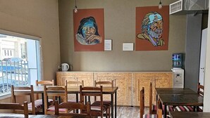 Een restaurant met houten tafels en stoelen, een houten toonbank en twee schilderijen aan de muur.