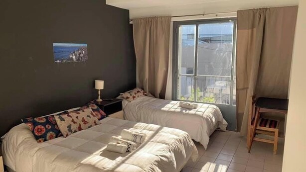 Een slaapkamer met twee bedden, een raam met gordijnen, een kleine tafel en een wandlamp.