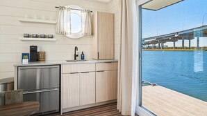 Cocina compacta con vistas a un puente sobre el agua, un refrigerador pequeño y una ventana con cortinas.