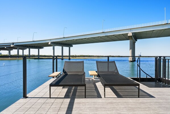 Terraza frente al río con sillas de descanso y una pequeña mesa, con vista a un puente.
