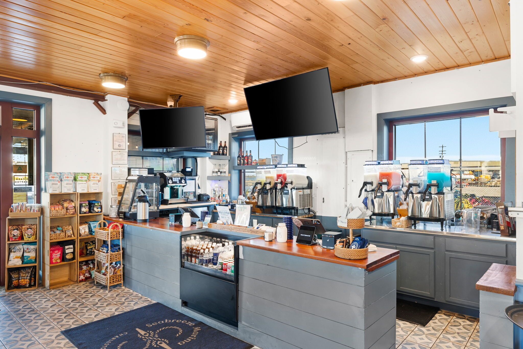 A cafe with a wooden ceiling, a counter with coffee machines, and a TV mounted above it.