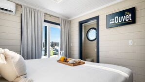Habitación de hotel con cama, bandeja de desayuno, cortinas, un cartel que dice "Stay Duvet" y ventana con vistas.
