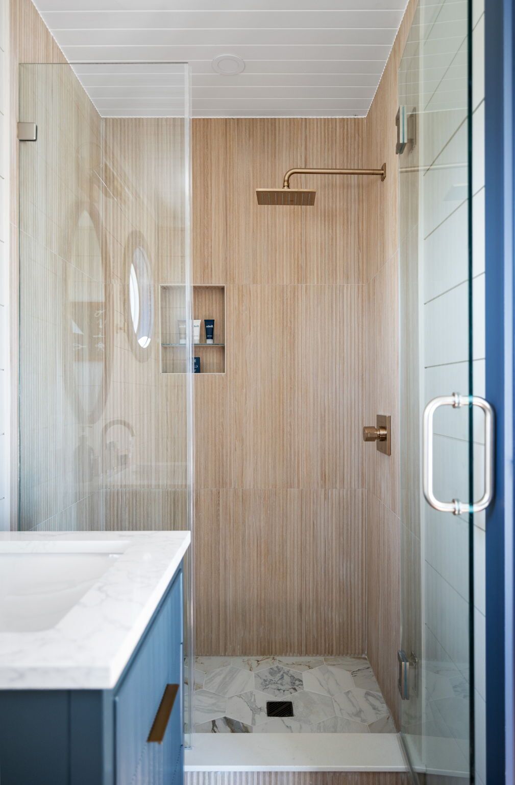 A modern bathroom with a shower, a vanity with a marble countertop, and a glass shower enclosure.