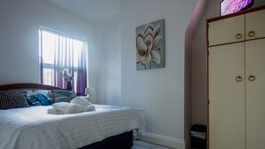 Een slaapkamer met een bed, een raam met gordijnen, een schilderij en een kledingkast.
