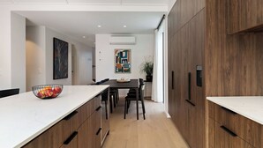 A modern kitchen with a white countertop, wooden cabinets, and a dining area with a table and chairs.