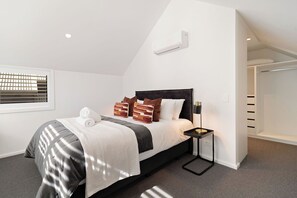 Un dormitorio moderno con cama, mesita de noche, ventana con persianas y armario empotrado.