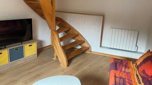 Een houten trap in een kamer met een televisie, een radiator en een kleurrijke bank.