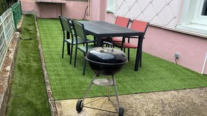 Een terras met een barbecue, een tafel en stoelen, en een klein stukje kunstgras.
