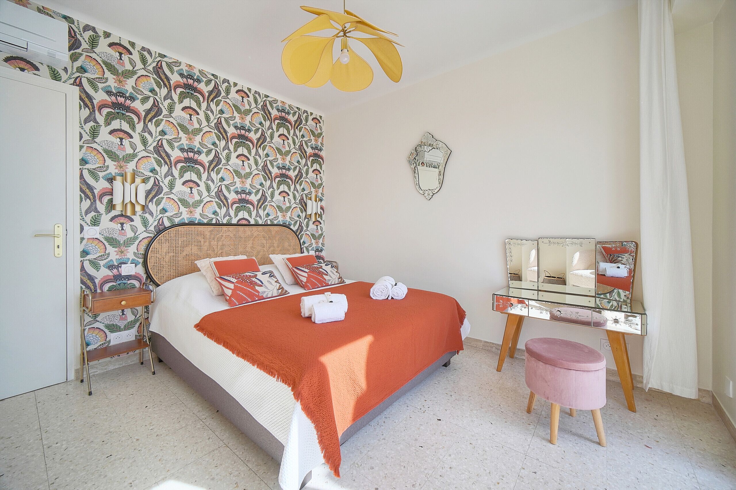 Ein Schlafzimmer mit Bett, Nachttisch, Schminktisch und einem kleinen Hocker.