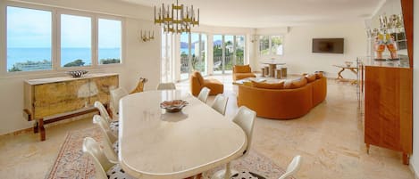 A spacious living room with a large dining table, a sofa, and a TV mounted on the wall.