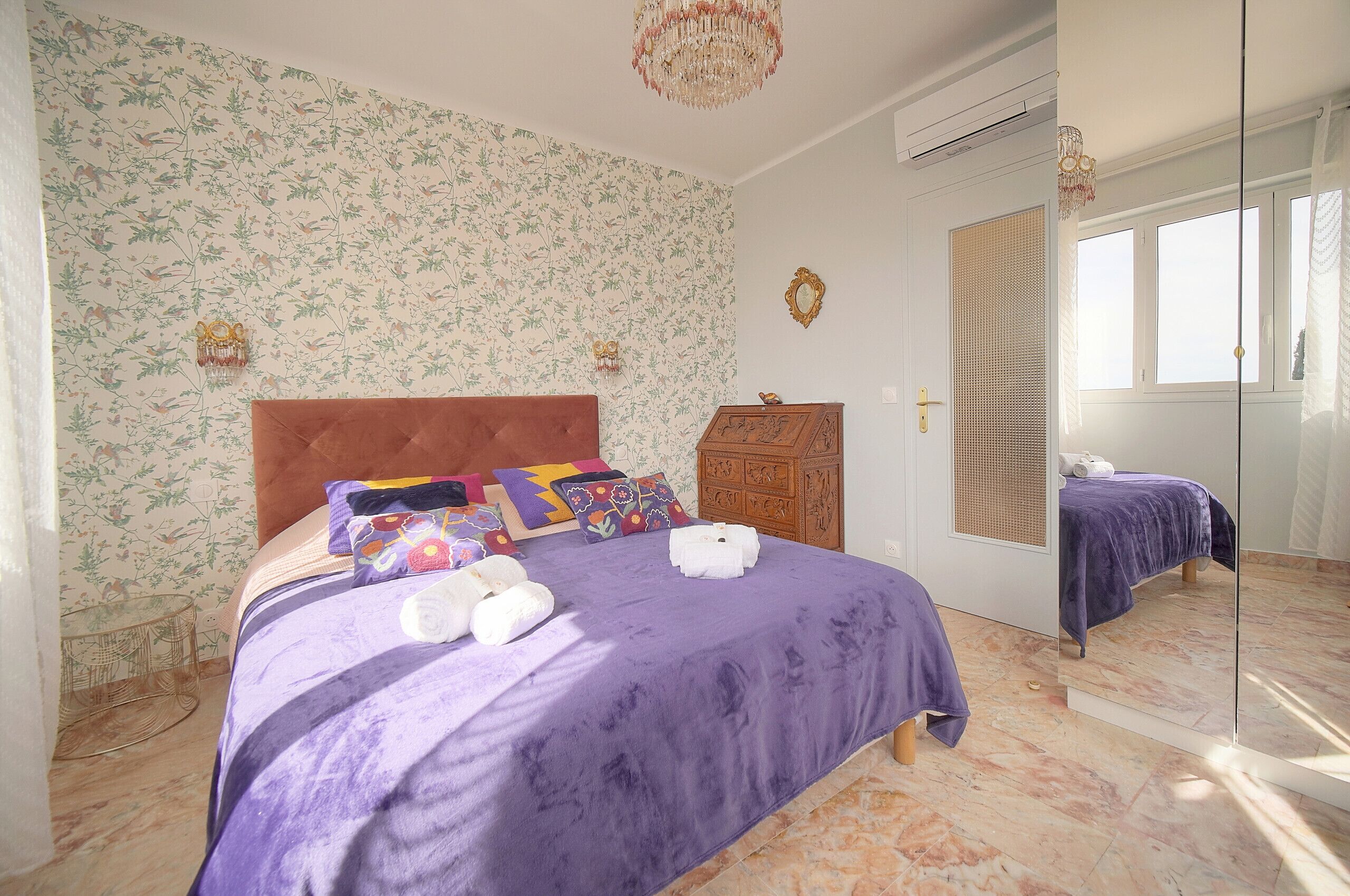 A bedroom with a purple bedspread, a wooden headboard, and a mirror cabinet.