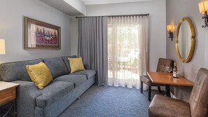 A hotel room with a grey sofa, yellow cushions, a wooden table with a chair, a mirror, and a painting on the wall. - Big Fun, Boutique Feel – Your Napa Getaway- Wyndham Vino Bello- Studio (Napa)