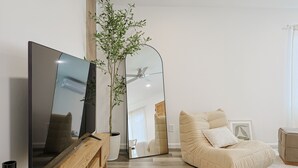 Un salon moderne avec un téléviseur à écran plat, un grand miroir, un canapé beige et une plante en pot.