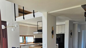 A spacious living area with a wooden floor, a dining table with chairs, and a kitchen in the background.
