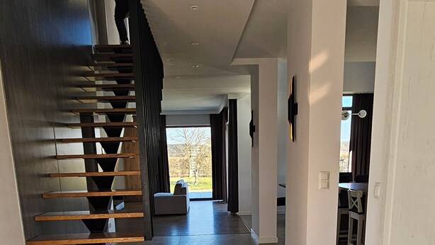 A modern interior with a central staircase, a dining area, and a view through an open space.