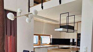 A modern kitchen with a central island, a dining area with a wooden table and chairs, and a staircase leading to an upper level.