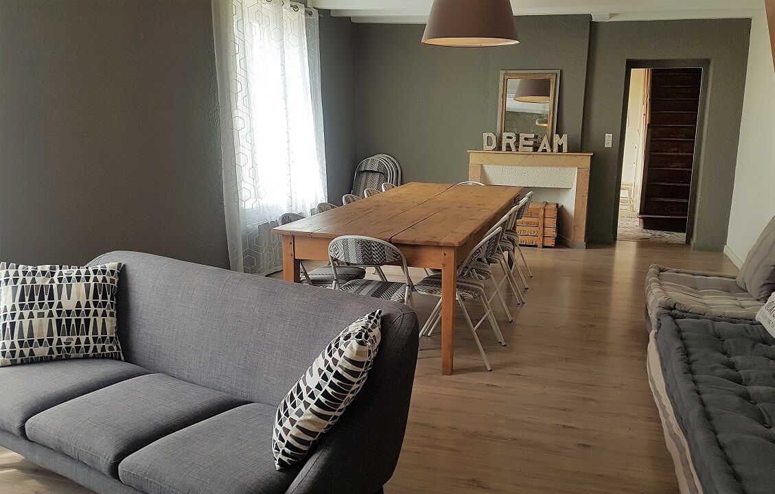 Ein modernes Wohnzimmer mit einem grauen Sofa, einem Holzespeisetisch mit Stühlen und einer Treppe zu einer weiteren Ebene.