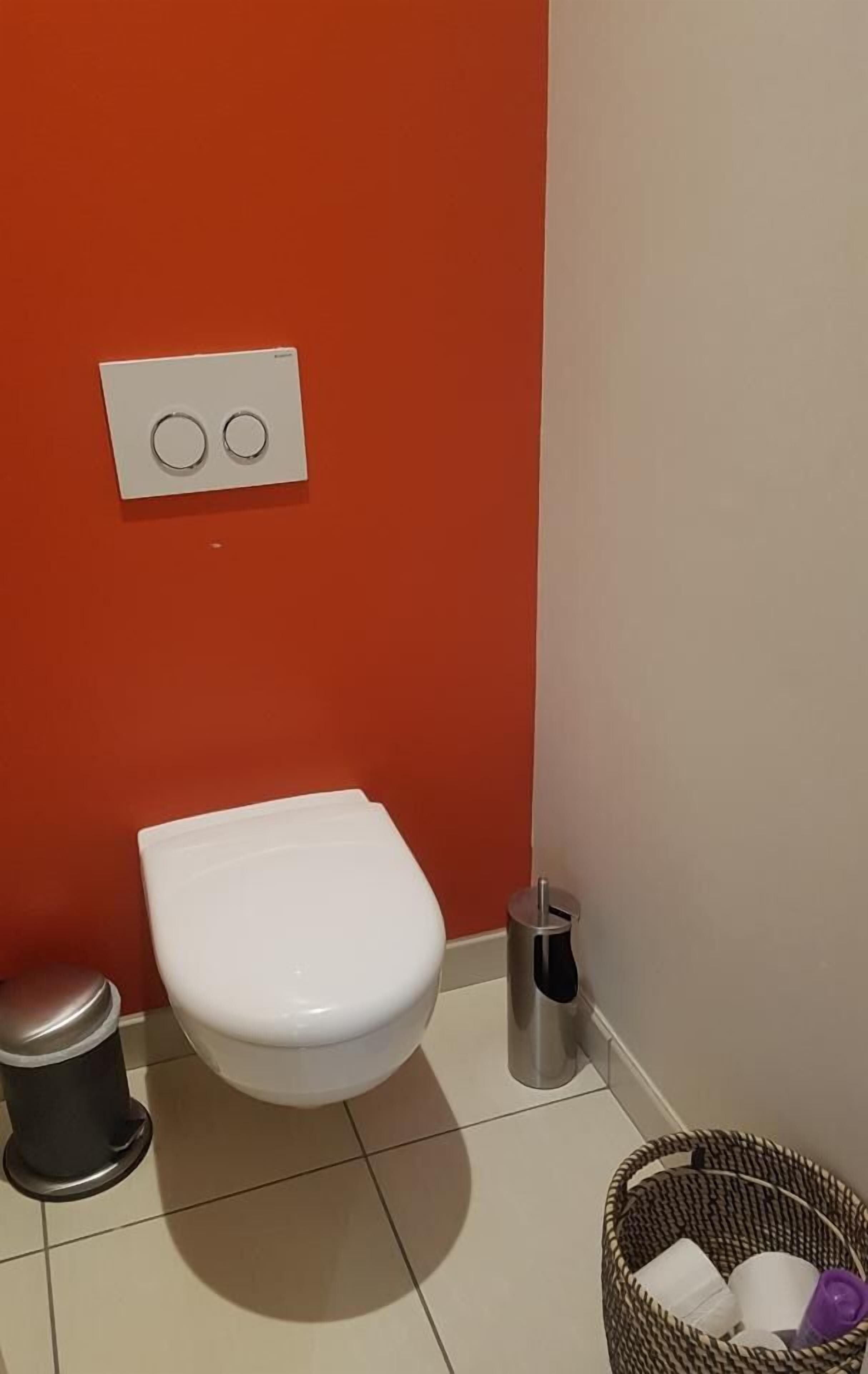 A bathroom with a white toilet, a trash bin, and a basket with toiletries.