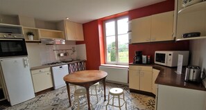 Eine kompakte Küche mit Gasherd, Mikrowelle und kleinem Kühlschrank. Ein Fenster sorgt für natürliches Licht und bietet Blick ins Grüne.