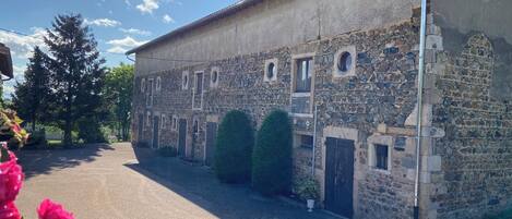 Un edificio de piedra con varias ventanas y puertas, un patio empedrado y un cielo despejado.