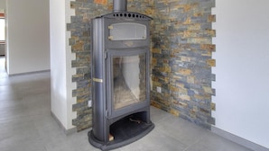 A modern wood-burning stove in a corner with a stone-patterned wall. - Gite du Bobet - CHAMBOST LONGESSAIGNE (CHAMBOST LONGESSAIGNE)