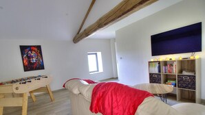 A room with a foosball table, a couch with a red blanket, a bookshelf, and a painting on the wall. - Gite du Bobet - CHAMBOST LONGESSAIGNE (CHAMBOST LONGESSAIGNE)