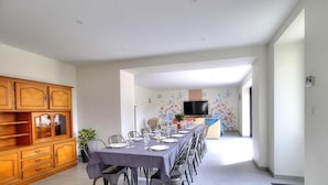 A dining area with a long table set for six, flanked by wooden cabinets and a TV in the background. - Gite du Bobet - CHAMBOST LONGESSAIGNE (CHAMBOST LONGESSAIGNE)