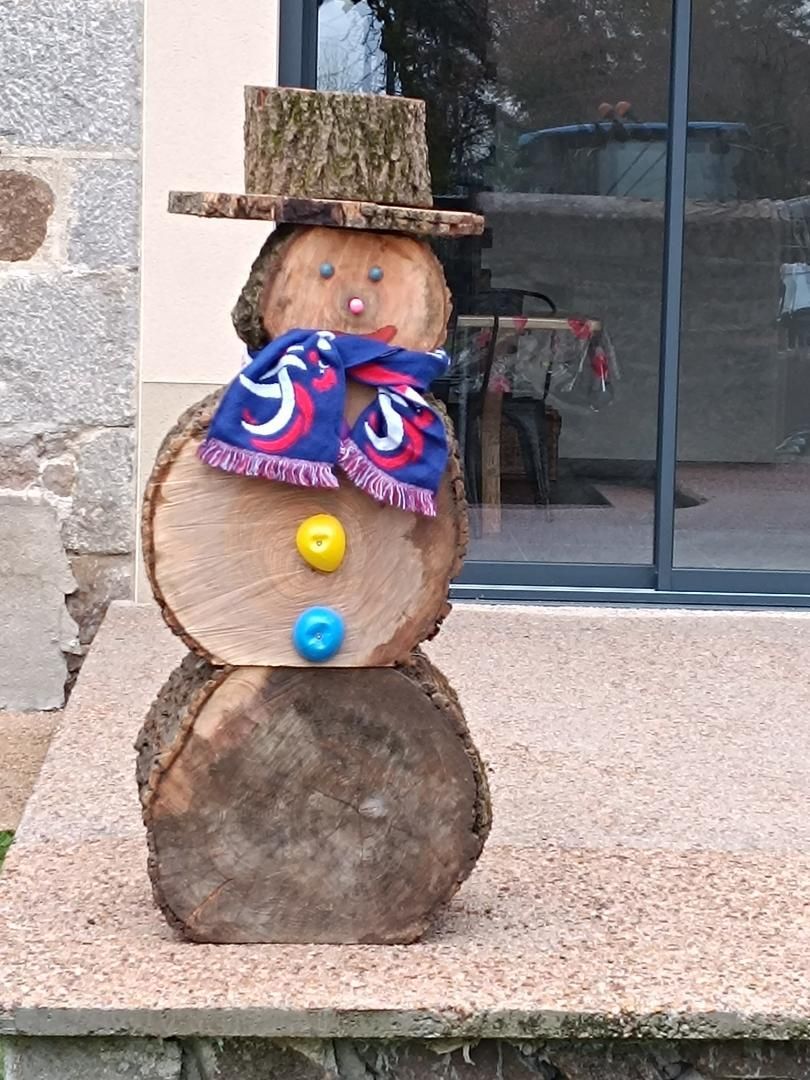 Een sneeuwpop van boomstammen met een hoed, sjaal en knopen.