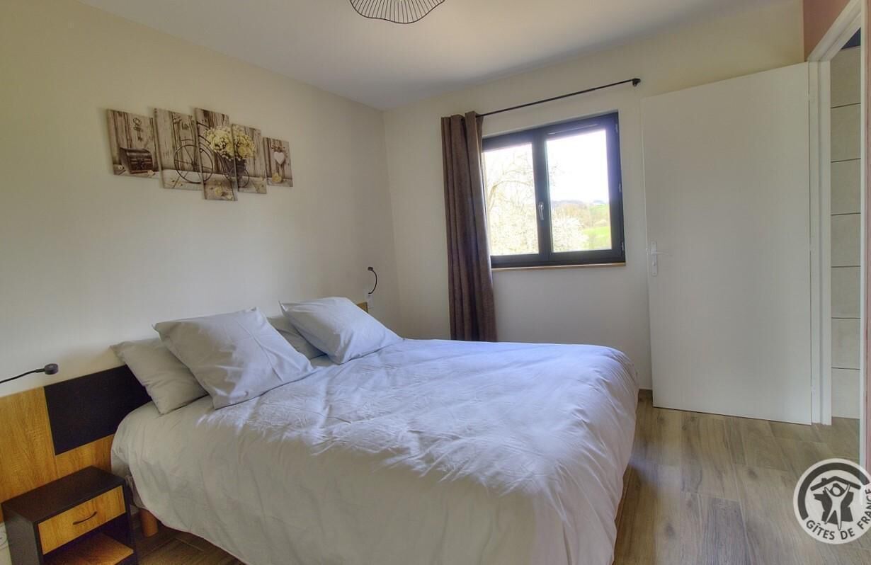 A bedroom with a bed, a nightstand, a window with curtains, and wall art.