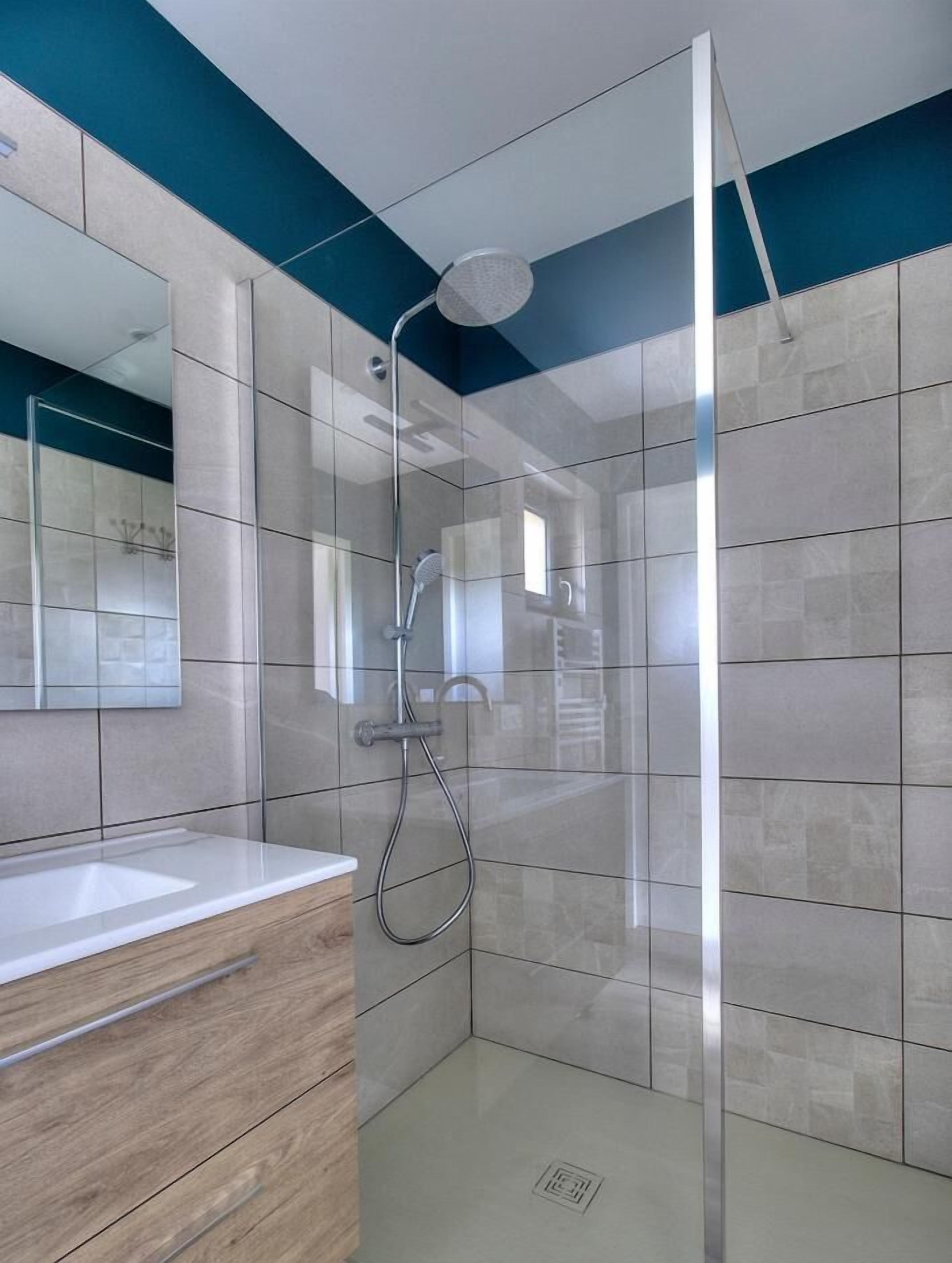 Een moderne badkamer met een douchecabine van glas, een houten wastafelmeubel en een grote spiegel.