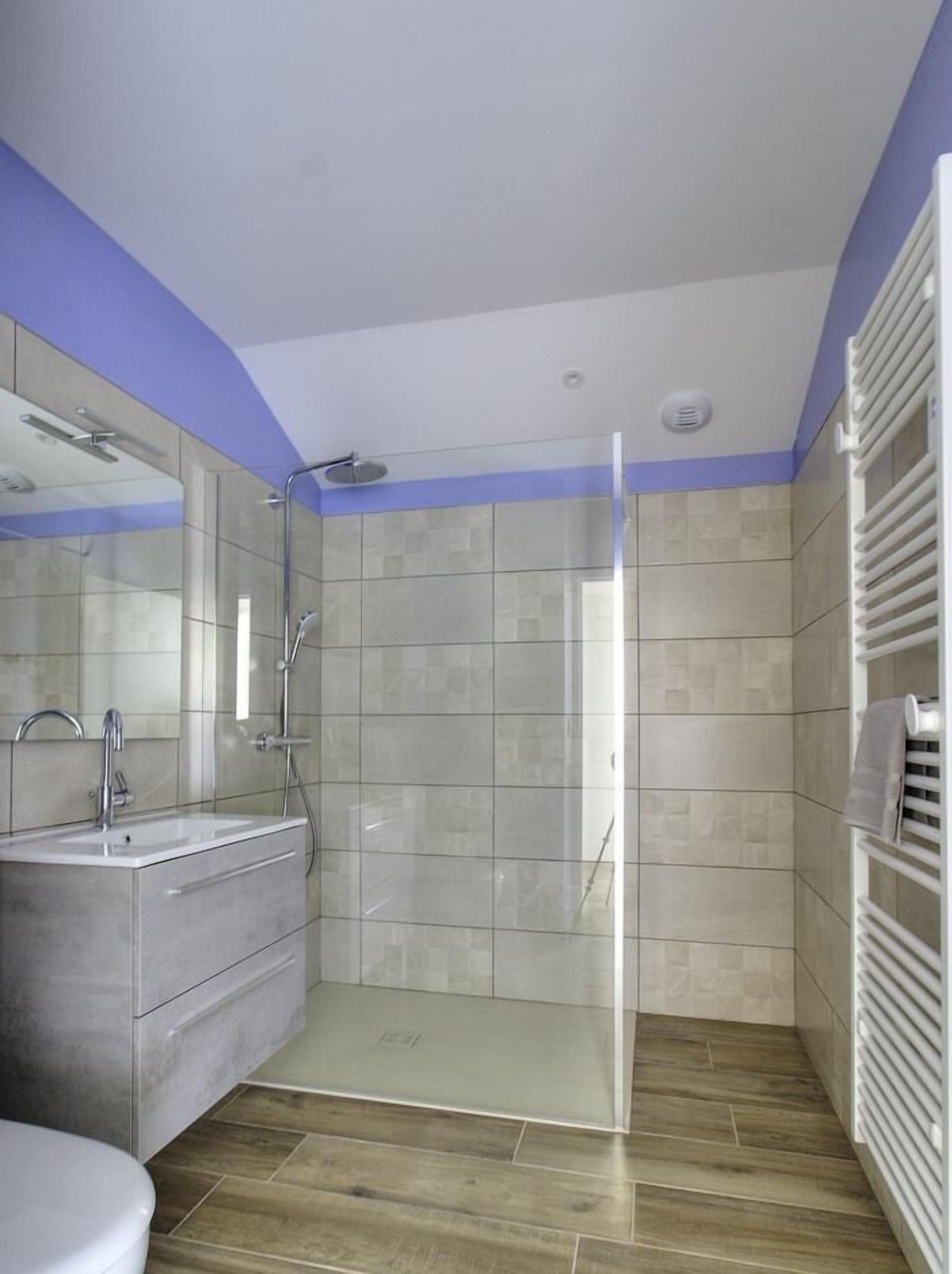 A modern bathroom with a glass-enclosed shower, a vanity with a sink, and a towel rack.