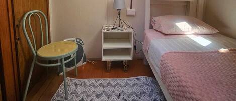 A cozy dormitory room with bunk beds, a small desk with a lamp, a chair, and a patterned rug.