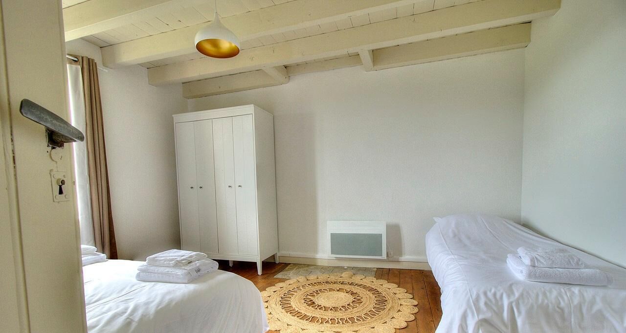 Une chambre avec deux lits, une armoire blanche, un luminaire au plafond et un petit radiateur.