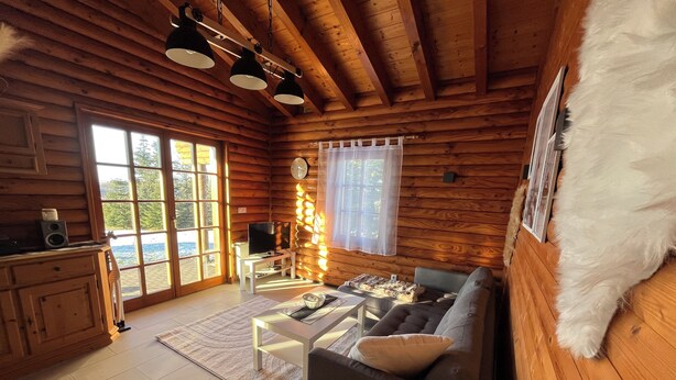 A cozy cabin with wooden walls, a sofa, a dining table, and a TV. - VACATION HOUSE VACATION APARTMENT EIFEL-ARDENNEN LOG CABIN VIEBIGHAUS (Buchet)