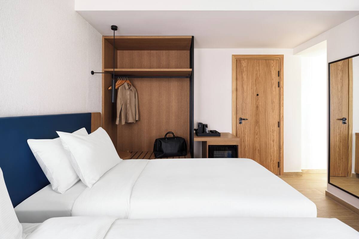 A modern hotel room with a large bed, a wardrobe, a desk with a chair, and a mirror.
