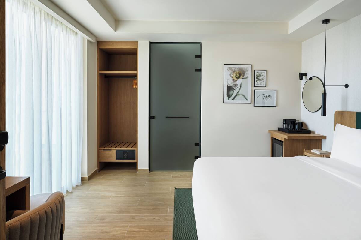 A hotel room with a bed, a desk, a chair, a wardrobe, and a small seating area.