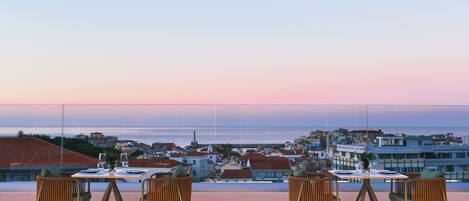 Piscina en la azotea con cuatro sillas de mimbre y una mesa, con vistas a un pueblo costero con edificios y un faro.