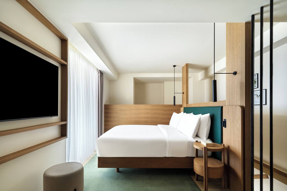 A modern hotel room with a large bed, a flat-screen TV, a small seating area, and a green rug.