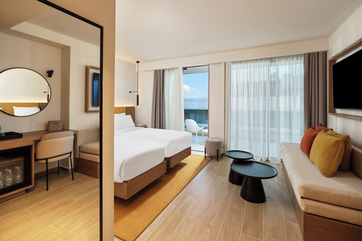 A hotel room with a bed, a desk, a chair, a sofa, two side tables, and a TV.