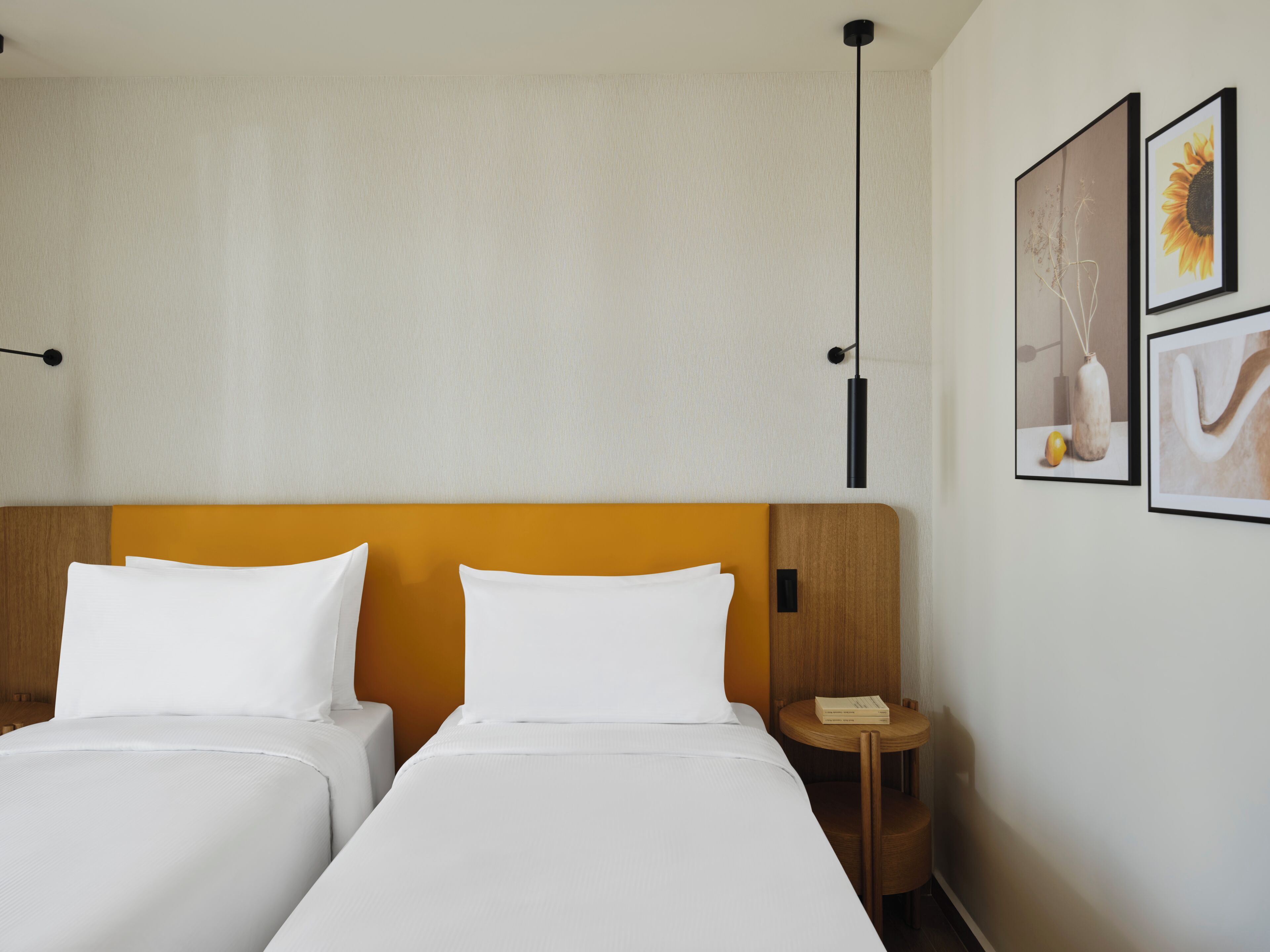 A hotel room with two beds, a wooden headboard, a nightstand, and two framed pictures on the wall.